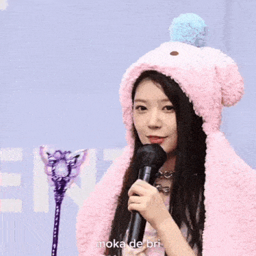 a woman wearing a pink hat and scarf is holding a microphone