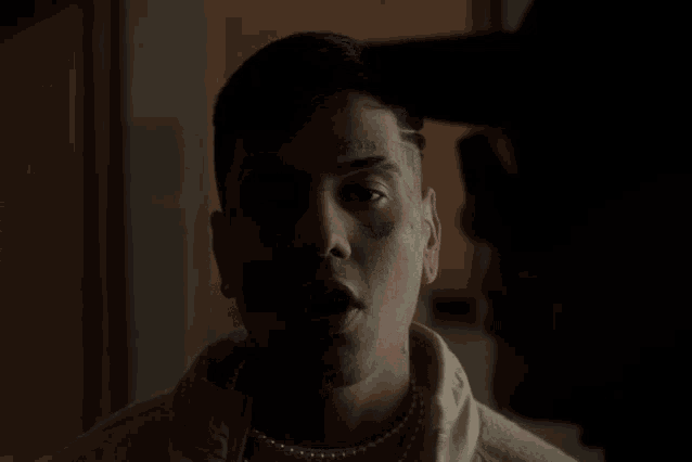 a man with a tattoo on his forehead looks at another man in a dark room
