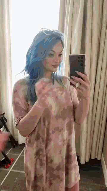a woman with blue hair is taking a selfie in the mirror .