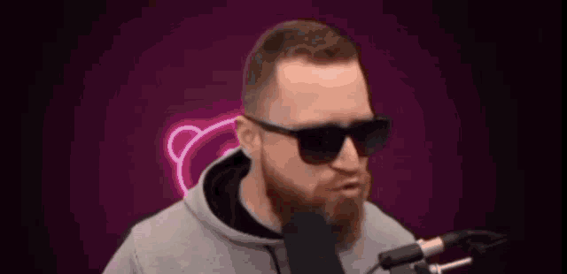 a man with a beard and sunglasses is standing in front of a microphone and saying cu .
