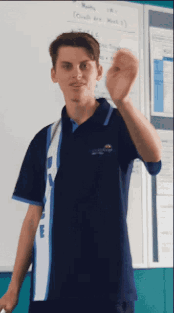 a young man wearing a blue shirt with the letter e on it stands in front of a white board
