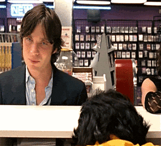 a man in a suit sits at a counter in front of a sign that says " new "