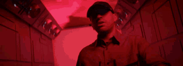 a man wearing a black hat and a red shirt is standing in a dark room