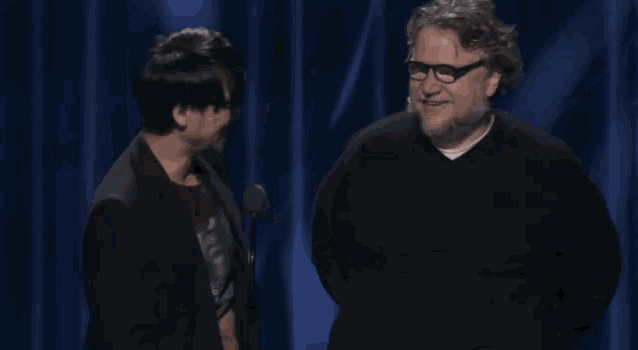 two men are standing next to each other on a stage with a microphone in front of them .