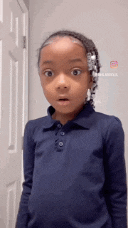 a young girl wearing a blue shirt is standing in front of a door .