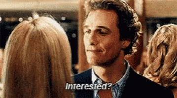 a man in a suit is talking to a woman and asking if she is interested in him .