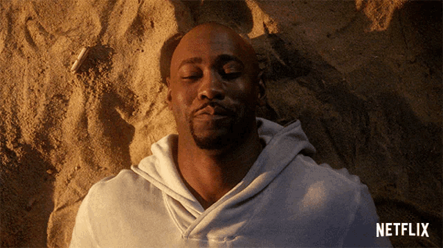 a man is laying in the sand with his eyes closed and a netflix logo above him