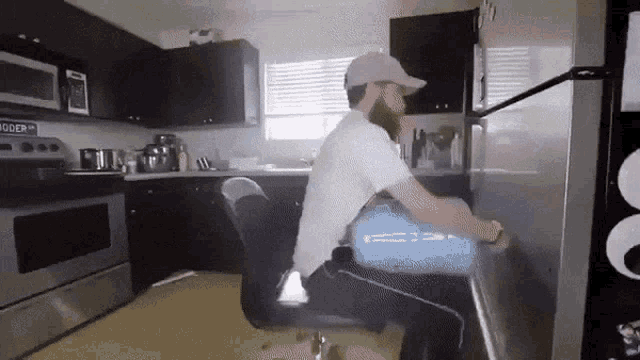a man is sitting in a chair in a kitchen with a sign that says " bigger "