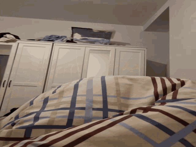 a bed with a plaid comforter and a white wardrobe
