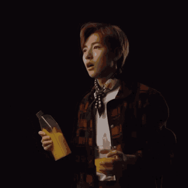 a man in a plaid jacket holds a bottle of orange juice and a glass of orange juice