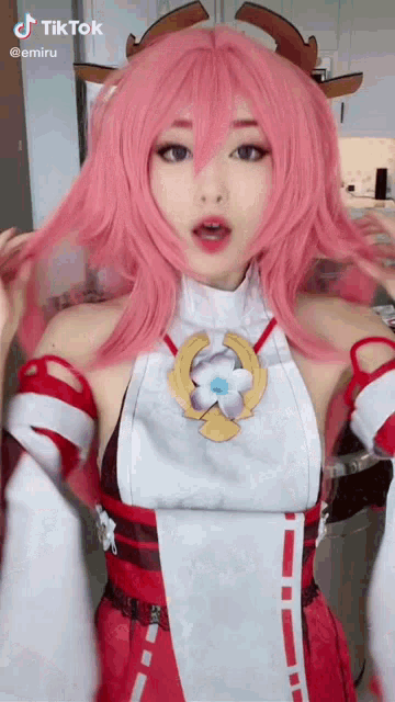 a woman wearing a pink wig and a red and white kimono is standing in a kitchen .