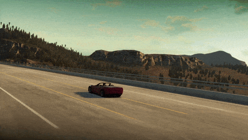 a red convertible car is driving down a road with mountains in the background