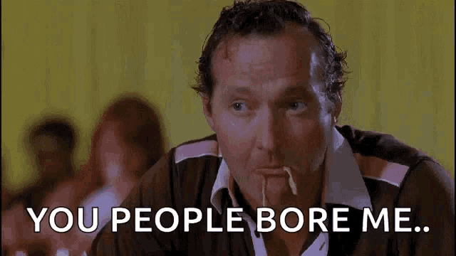 a man with a toothpick in his mouth is sitting at a table with the words `` you people bore me '' written above him .