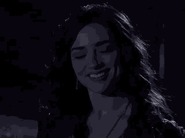a woman is smiling in the dark with her eyes closed and her hair blowing in the wind .