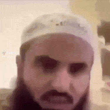 a man with a beard is wearing a white hat and has a tiktok sticker on his face .
