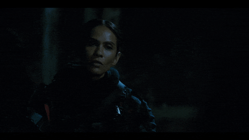 a woman in a black jacket stands in the dark looking at the camera