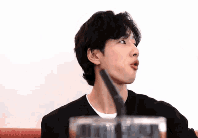 a man in a black sweater is drinking from a glass with a straw .