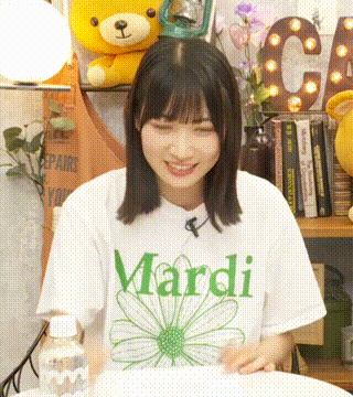 a young woman wearing a white mardi t-shirt is sitting at a table with a bottle of water .