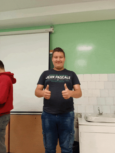 a young man wearing a jean pascale t-shirt gives a thumbs up