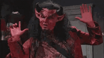 a man dressed as a devil with horns is standing in a room with his hands up .