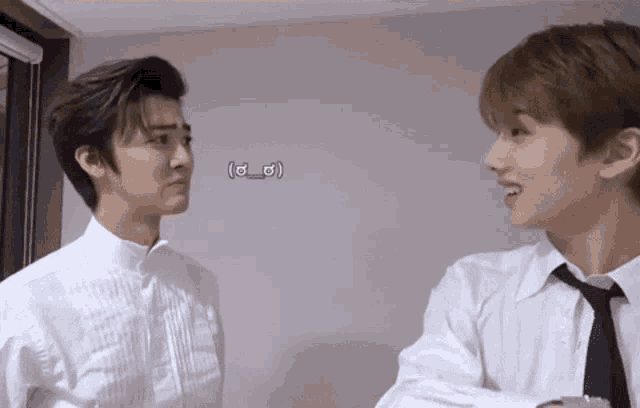 two young men in white shirts and ties are standing next to each other and looking at each other .
