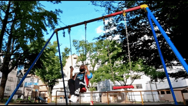 a person sitting on a swing in a park wearing a shirt that says ' spiderman ' on it