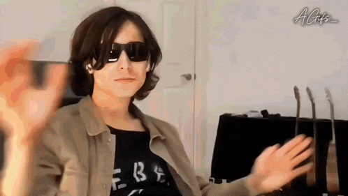 a man wearing sunglasses and a black shirt is waving his hand in front of a guitar .