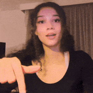 a woman in a black shirt is pointing her finger at the camera