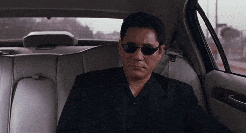 a man wearing black sunglasses sits in the back seat of a car