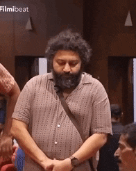 a man with a beard is kneeling down with his hands folded in front of a group of people .