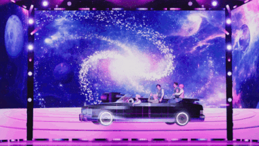a group of people sitting in a car on a stage with a galaxy in the background