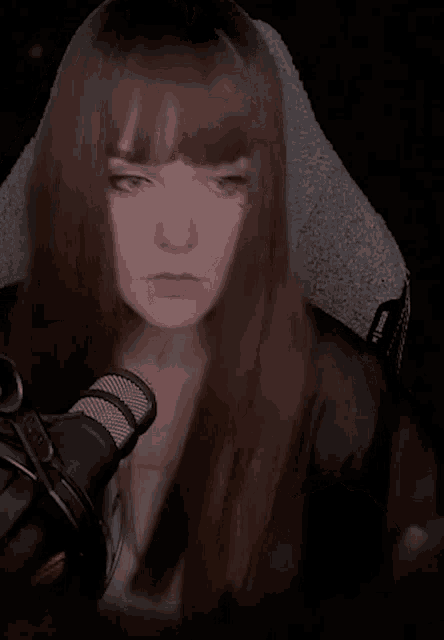 a woman with long brown hair is sitting in front of a microphone with her eyes closed