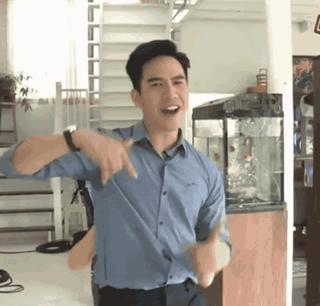 a man in a blue shirt is dancing in front of a fish tank