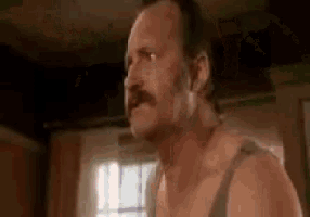 a man with a mustache is standing in a room without a shirt .
