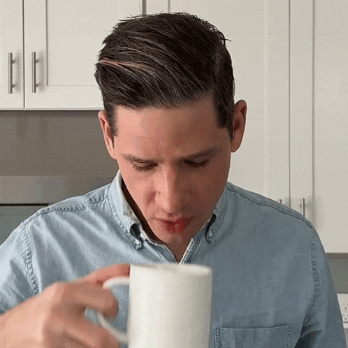 a man in a blue shirt drinks from a white mug