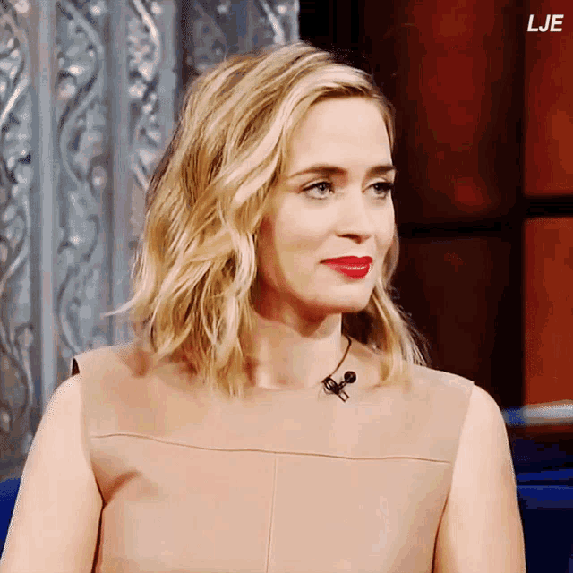 a woman with blonde hair and red lipstick is sitting in front of a red wall with the letters lje on the bottom
