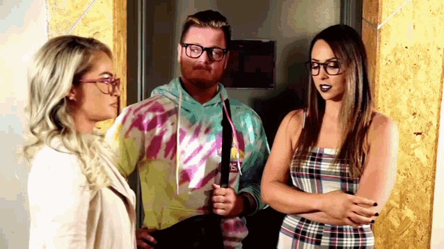 a man in a tie dye sweatshirt stands between two women wearing glasses .