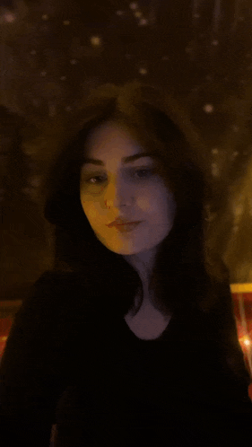 a woman in a black shirt is standing in front of a wall with lights on it
