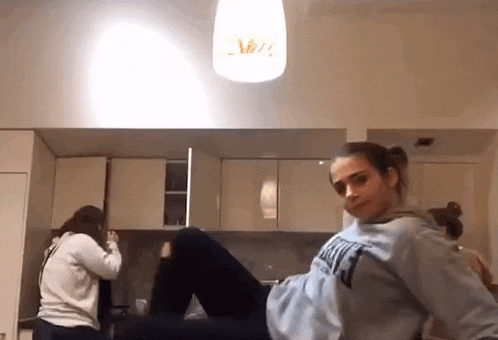a woman in a blue sweatshirt is sitting on the floor in a kitchen .
