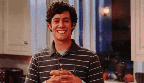 a young man in a striped shirt is smiling with his hands folded .