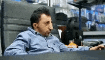 a man in a blue shirt is sitting at a desk with a remote control .