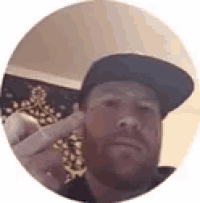a man with a beard is wearing a hat and holding his finger to his ear .