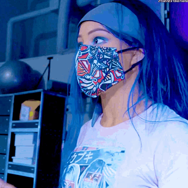 a woman with blue hair wearing a face mask with the next thing written on the bottom right