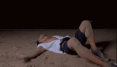 a man is laying on his back on the beach with his legs crossed
