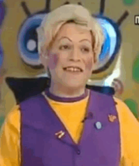 a woman is wearing a yellow shirt and a purple vest and smiling .
