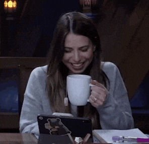 a woman is sitting at a table drinking a cup of coffee .