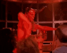 a man with horns is covered in red paint while holding a stick .