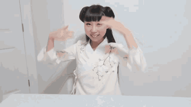 a woman in a white shirt is sitting at a table with her hair in two buns .