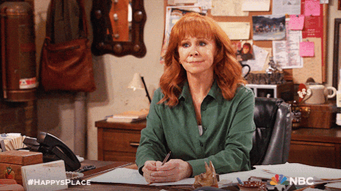 a woman in a green shirt sits at a desk with the hashtag #happysplace on the bottom