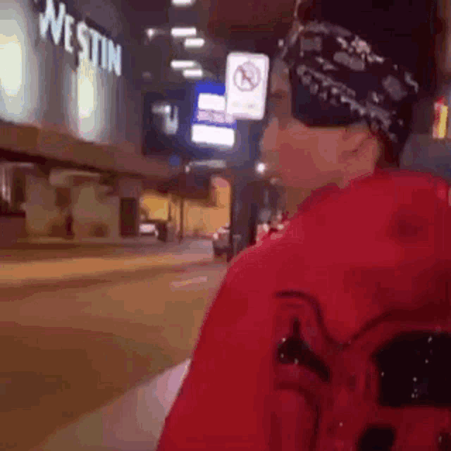 a man wearing a bandana and sunglasses is walking down a street in front of a westin hotel .